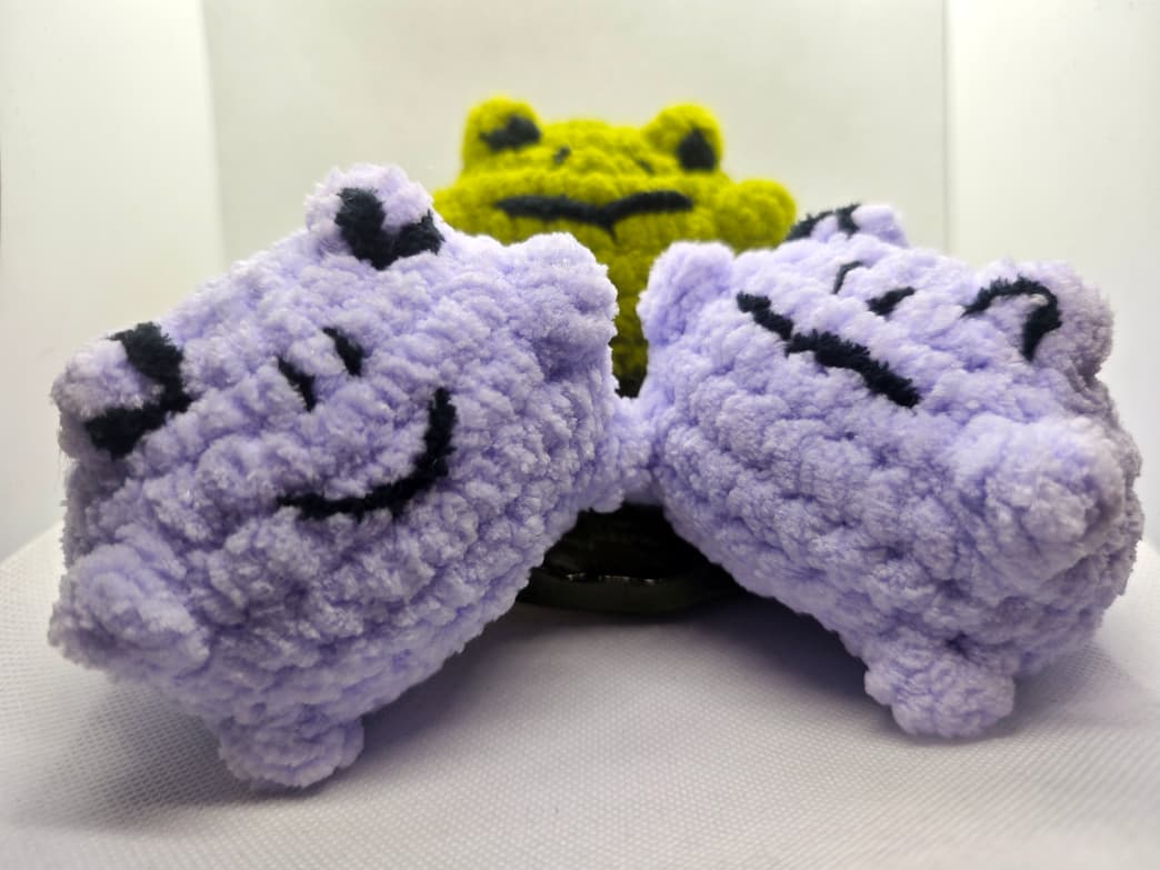 Handmade crochet cat plush toys in purple with green frog in background