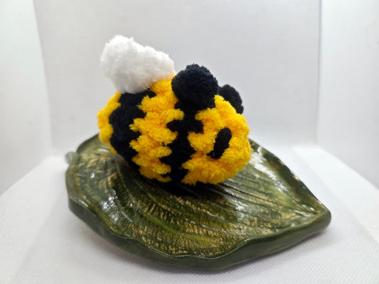 Side view of handmade crochet bee plush toy on decorative leaf dish