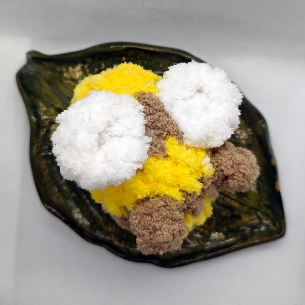 Top view of handmade crochet bee plush toy in yellow and brown with fluffy white wings