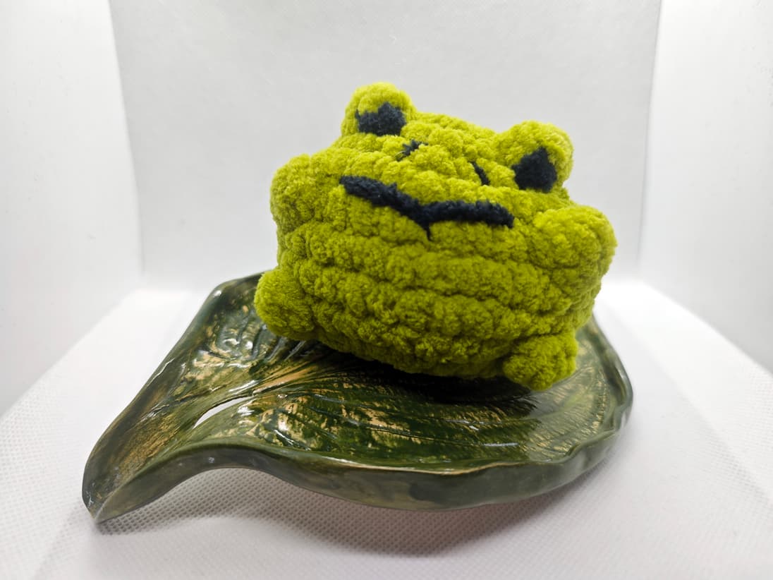 Handmade green crochet frog plush toy sitting on leaf dish