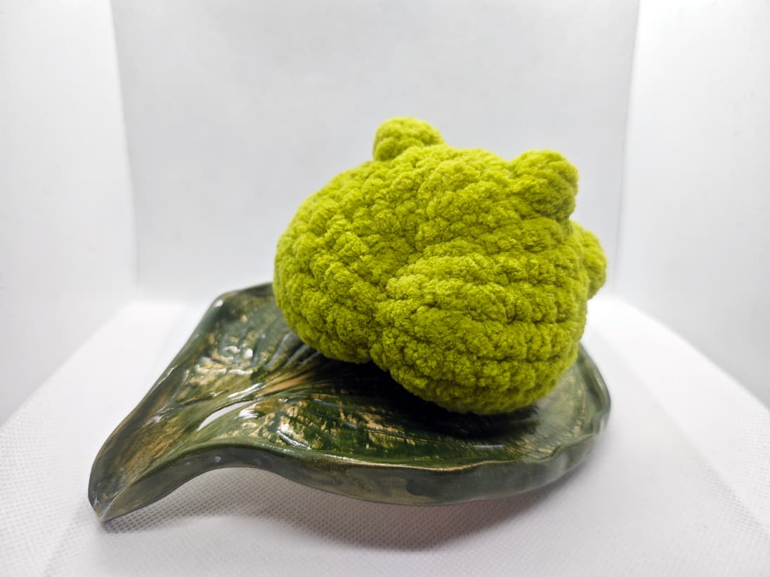 Handmade green amigurumi frog plush toy side view on decorative leaf dish