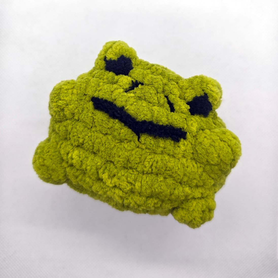 Close-up of handmade green crochet frog plush with embroidered face