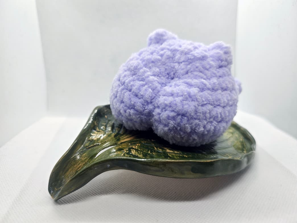 Back view of handmade purple crochet frog plush toy on leaf dish
