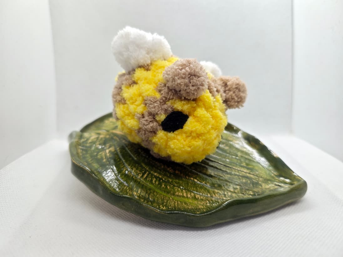 Handmade yellow and brown crochet bee plush toy with soft texture on leaf dish