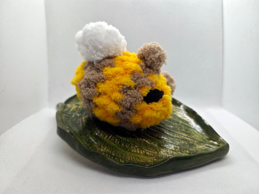 Handmade crochet bee plush toy in yellow and light brown on decorative leaf plate